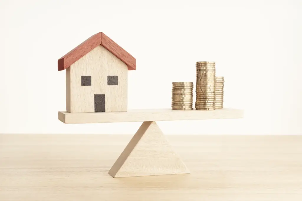 Symbolbild: Haus und Münzstapel auf Waage – Kosten für Hausverwaltung im Gleichgewicht
